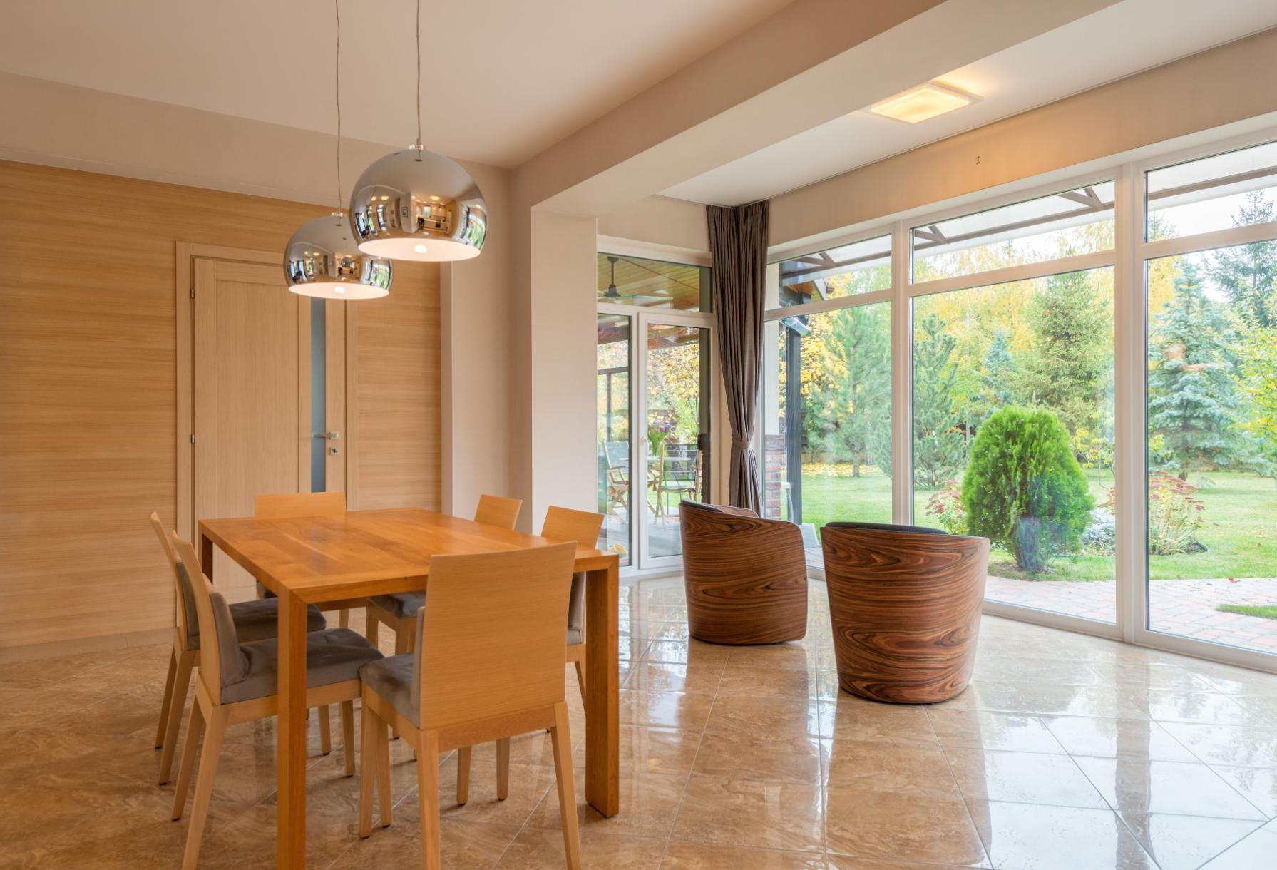 Bright dining area with wooden table, chairs, and large glass doors opening to a garden.