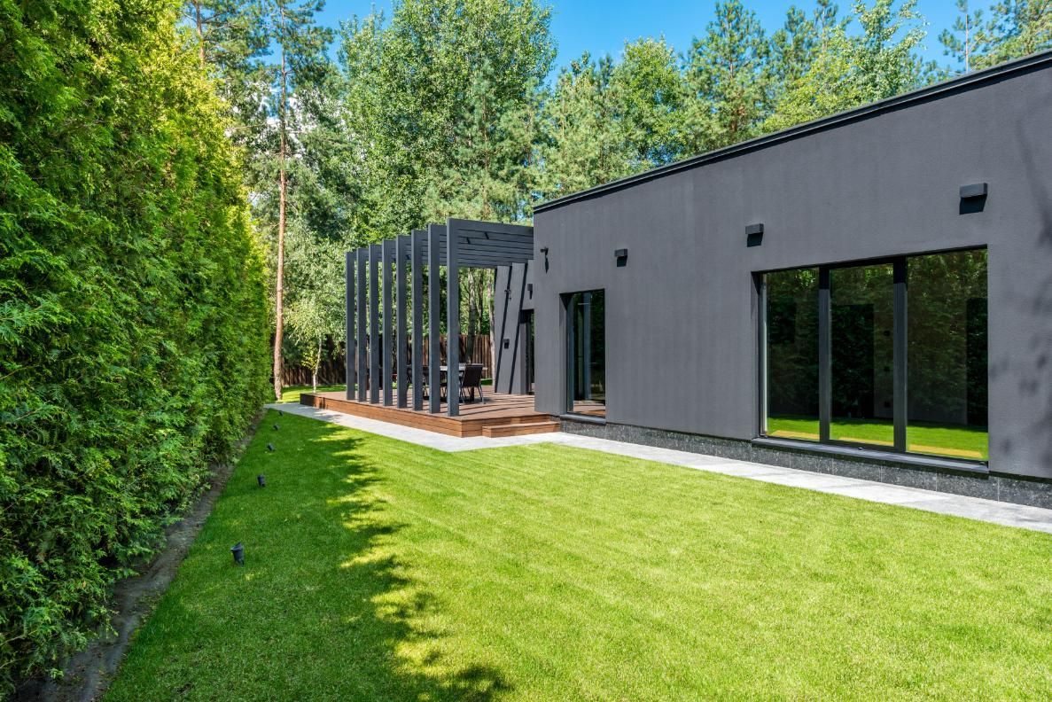Modern gray house with large windows beside a green lawn and tall trees