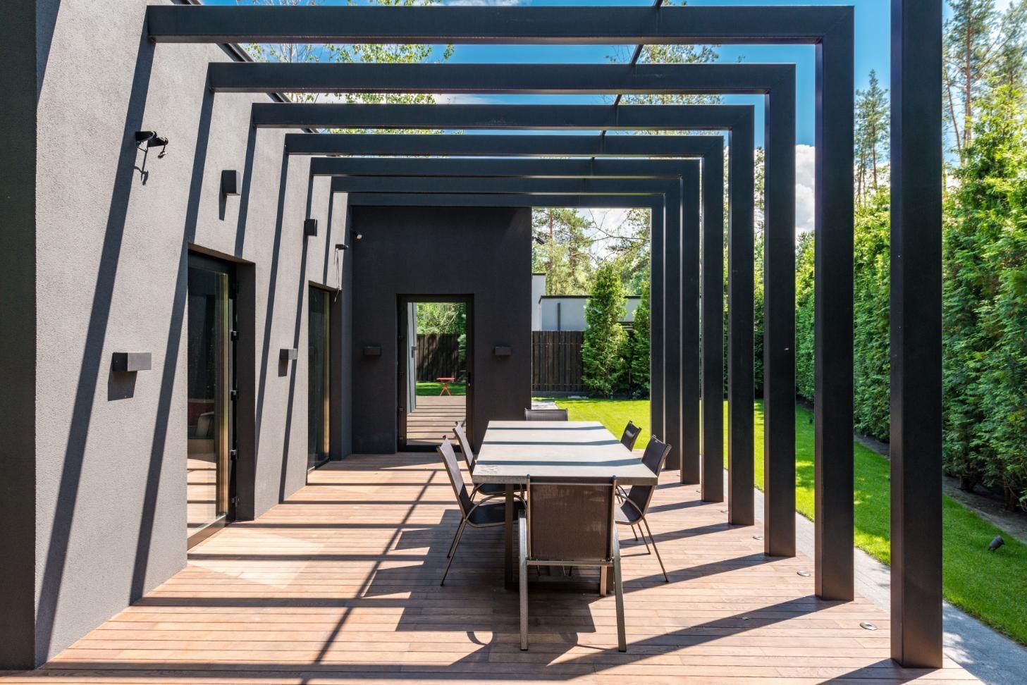 Modern outdoor patio with geometric black pergola, dining table, and chairs beside a green lawn.