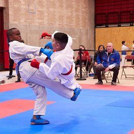 Two men are practicing karate in front of a black background.