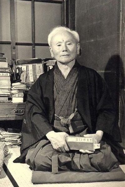 A black and white photo of a man in a kimono holding a book