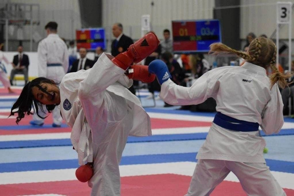 Two karate fighters are fighting on a mat in a gym.