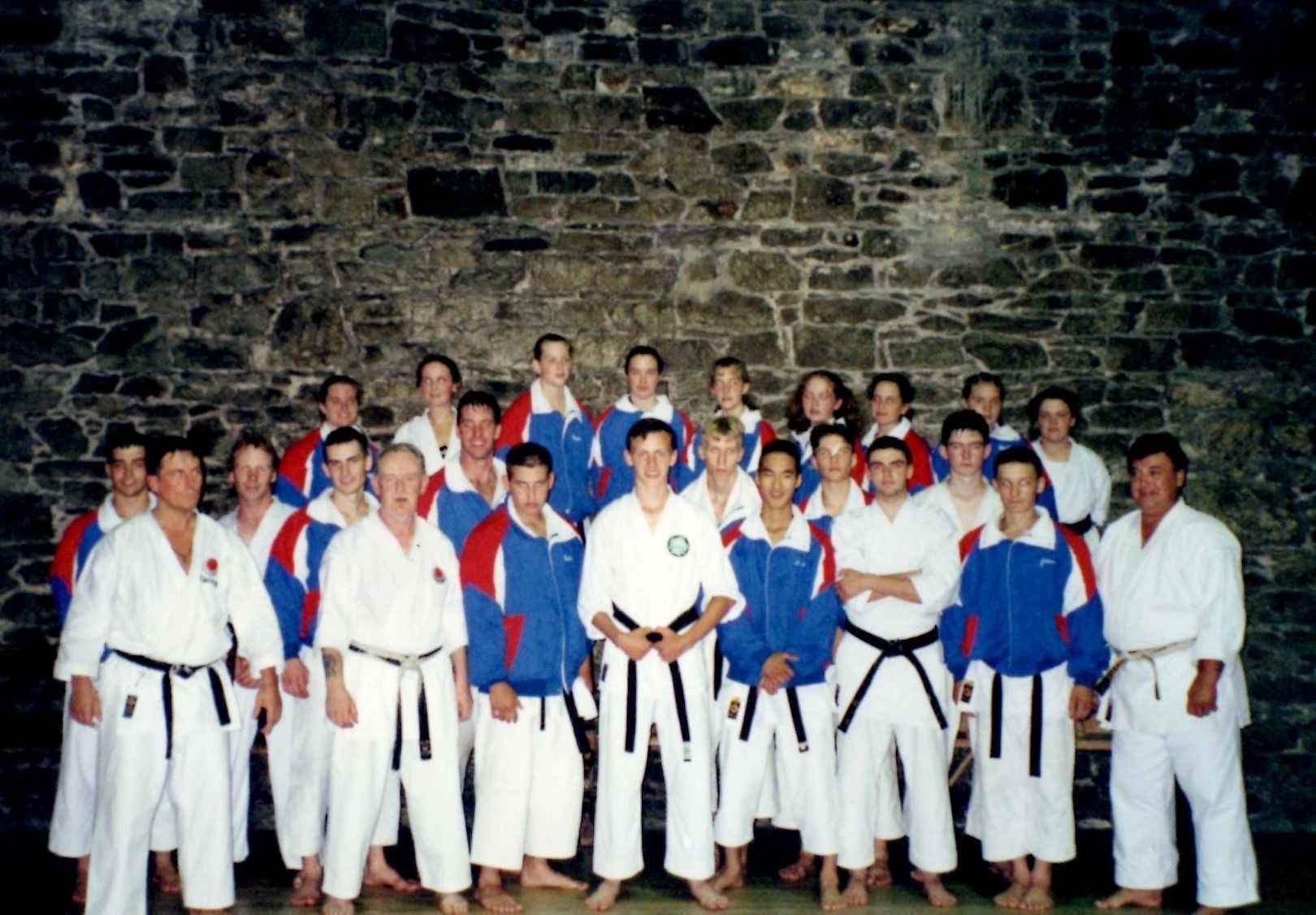 A group of karate fighters pose for a photo in front of a stone wall