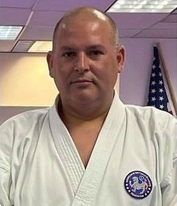 A man in a white karate uniform is standing in front of an american flag.