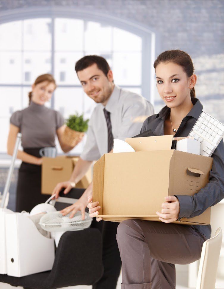 A team of movers, featuring 2 women and a man packing office items into brown cardboard moving boxes.