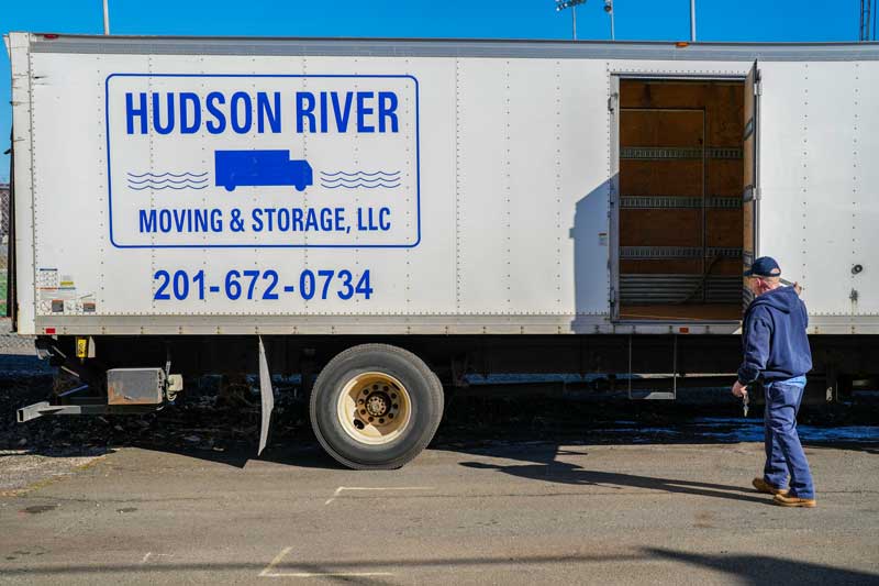 A Hudson River Moving & Storage truck and an employee closing the door, with the logo and and phone number listed on the side.