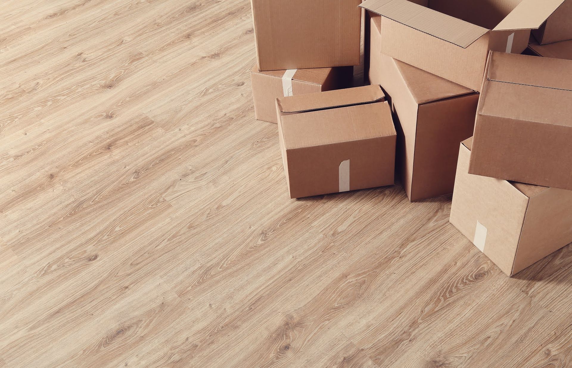 Empty brown cardboard moving boxes on a barren light brown wooden floor.