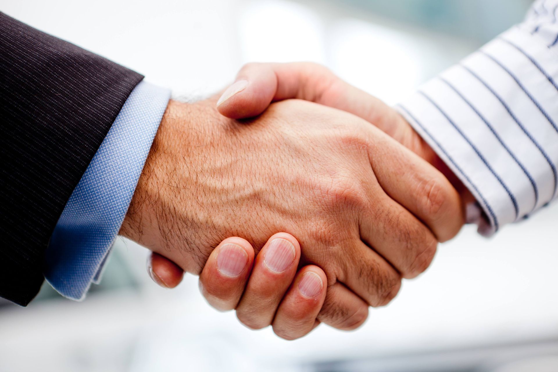 A close-up shot of a handshake between two men, one wearing a horizontally striped shirt, and another in a jumper.