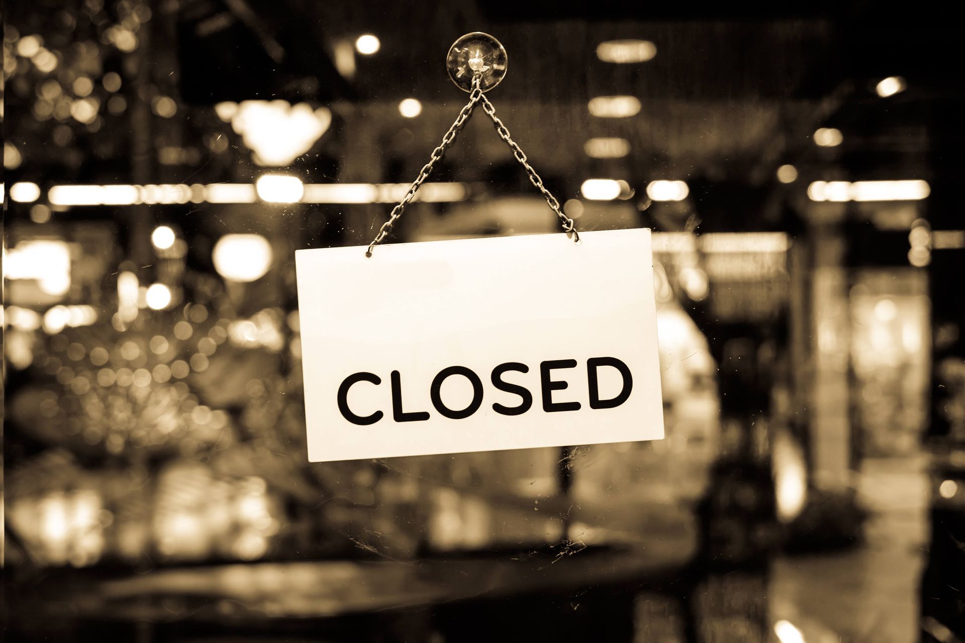 An image of a closed sign on the door of a business. The lights are on, showcasing indoor furniture and chandeliers.