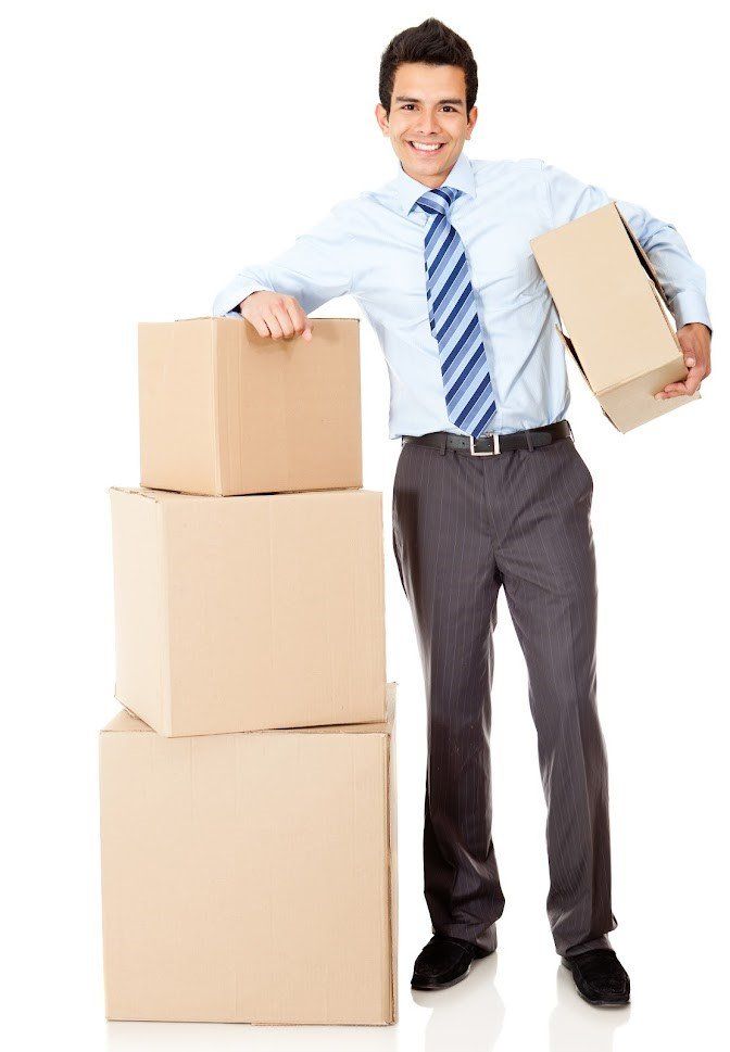 A man wearing a suit, with a blue shirt, blue tie, and vertically striped navy trousers, next to 3 brown cardboard boxes.
