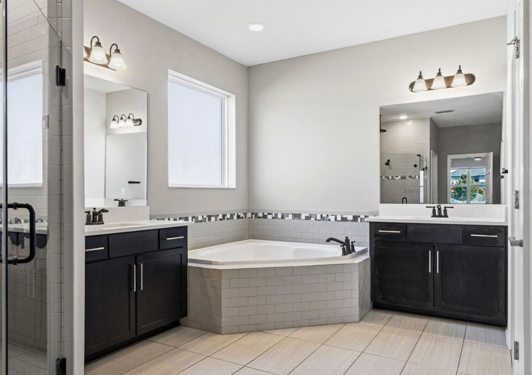 Bathroom with gray walls, dark cabinets, a corner tub, and a window.