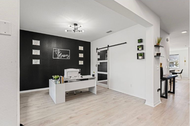 Modern office with white desk, black accent wall with awards, and sliding glass door.
