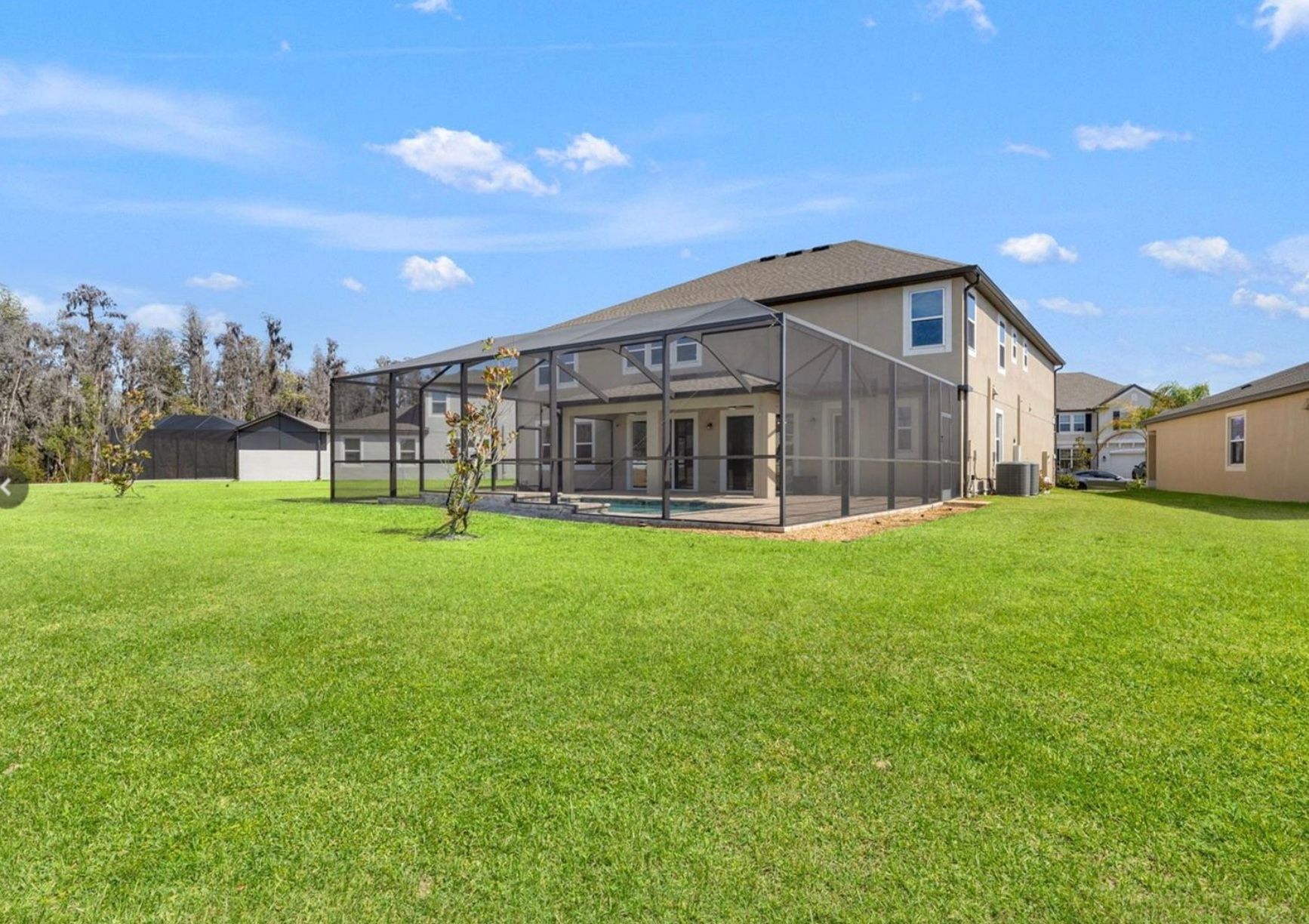 Backyard of a two-story house with a screened-in pool, shed, and green lawn under a blue sky.