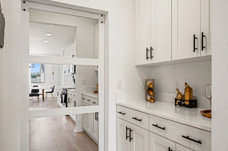 Hallway with pantry and white cabinets, glass door looking into kitchen.