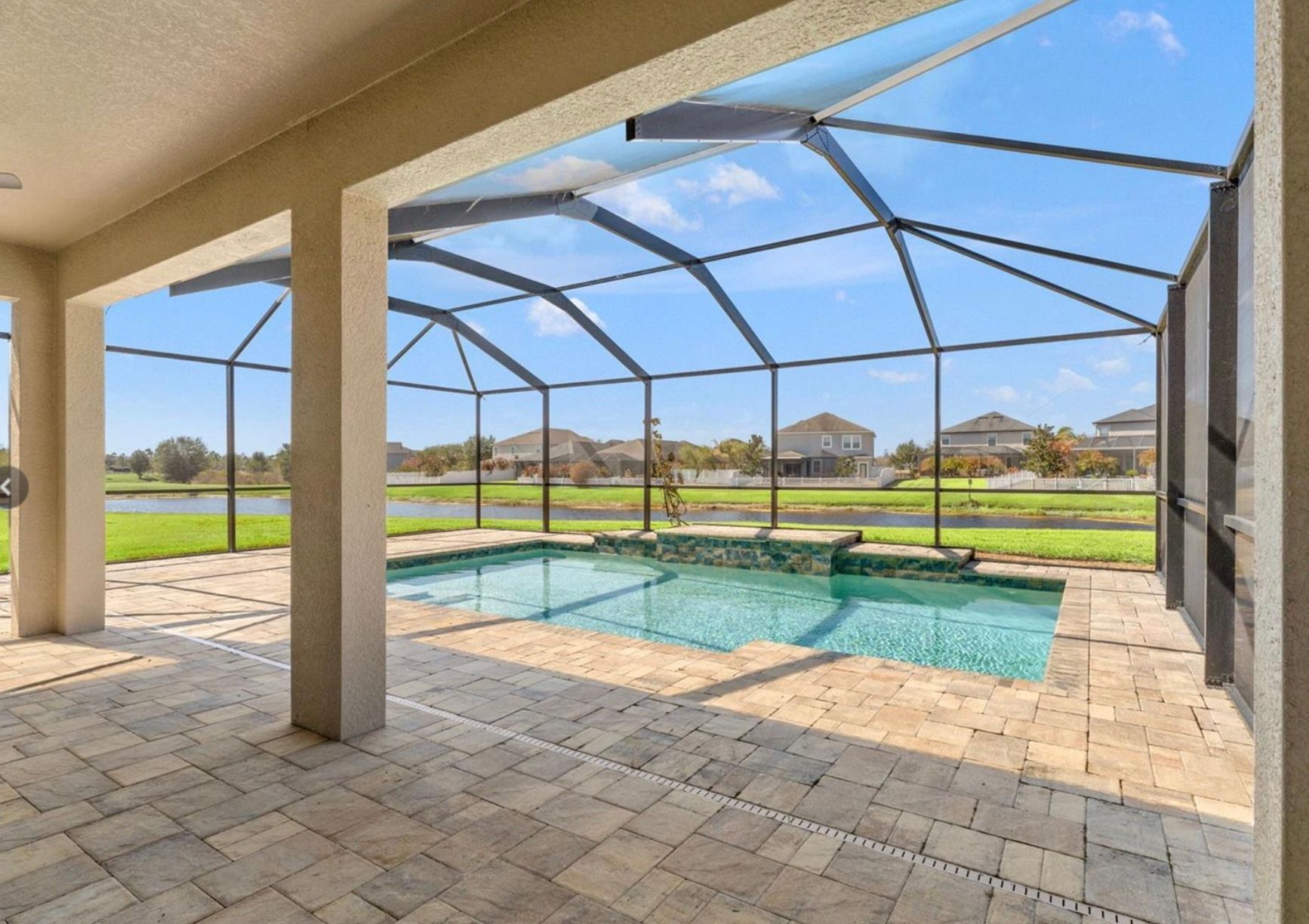 Covered patio with pool overlooking a lake, under blue sky.