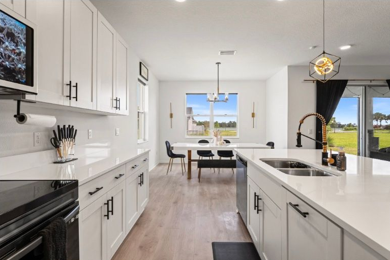 Modern white kitchen with island, dining table, and large windows.