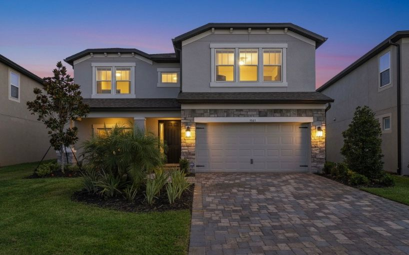 Two-story gray house with stone accents and a paver driveway at dusk.