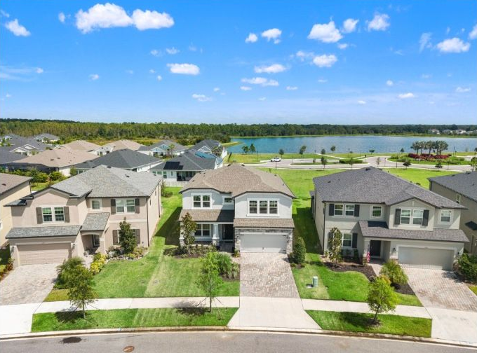 Aerial view of houses in a suburban neighborhood with a lake in the background under a blue sky.
