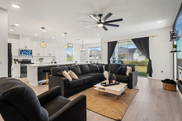Modern living room with dark gray sectional, open to a kitchen with white cabinets.