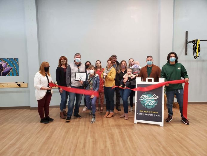 A group of people are cutting a red ribbon in a gym.