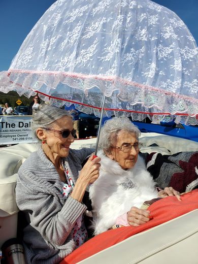 Two elderly women are sitting in a convertible car under an umbrella.