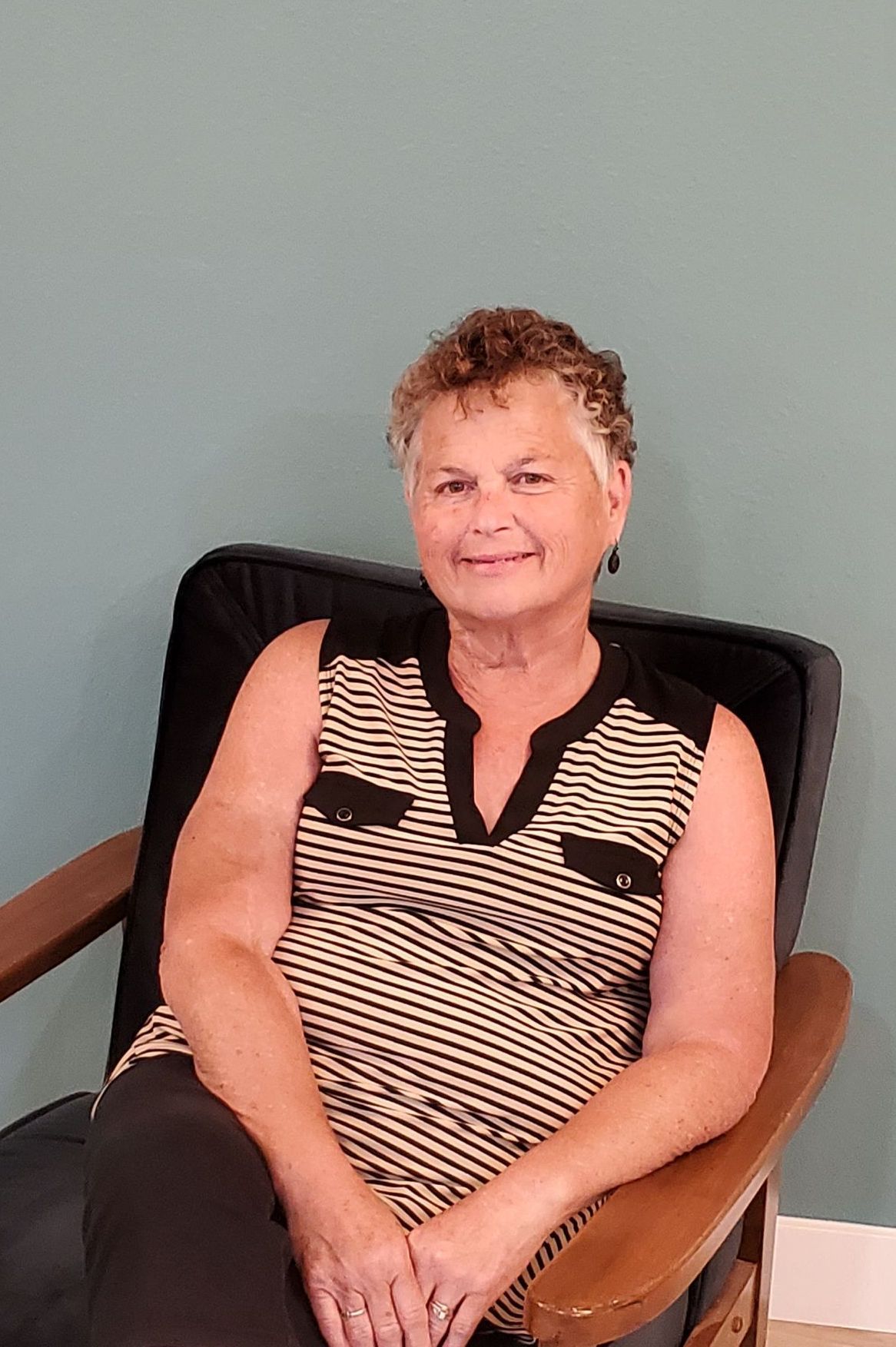 A woman in a no sleeve striped knit shirt and black bottoms. Short curly hair.