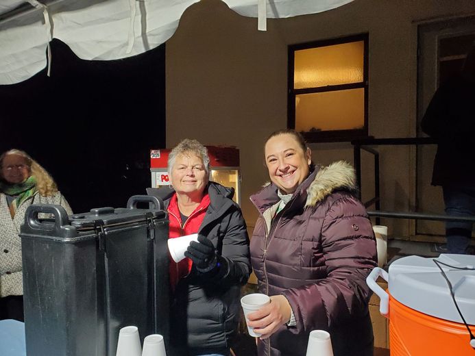 Two women are standing next to each other holding cups of coffee.