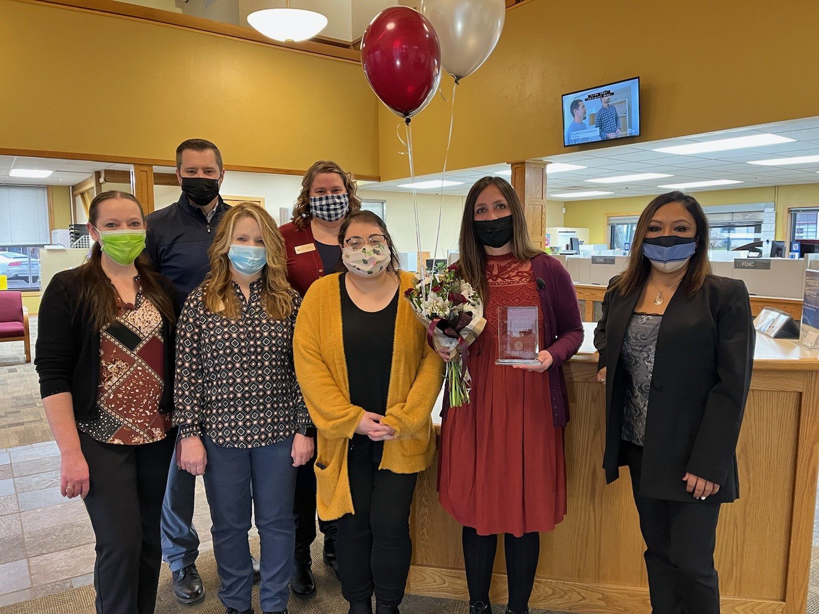 A group of people wearing face masks are posing for a picture in a bank.