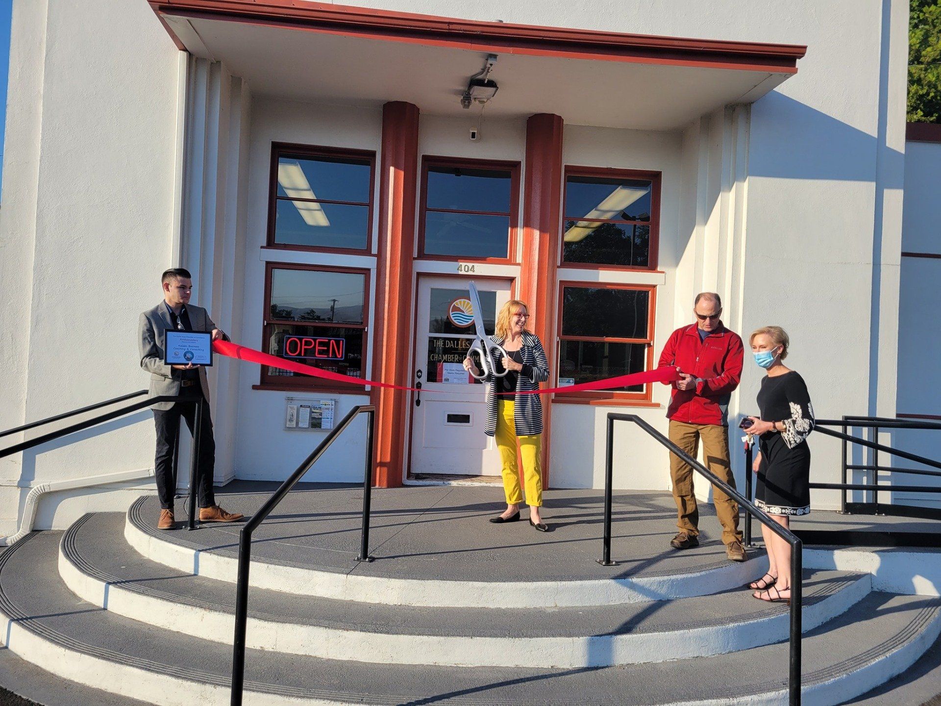 A group of people are cutting a red ribbon in front of a building.