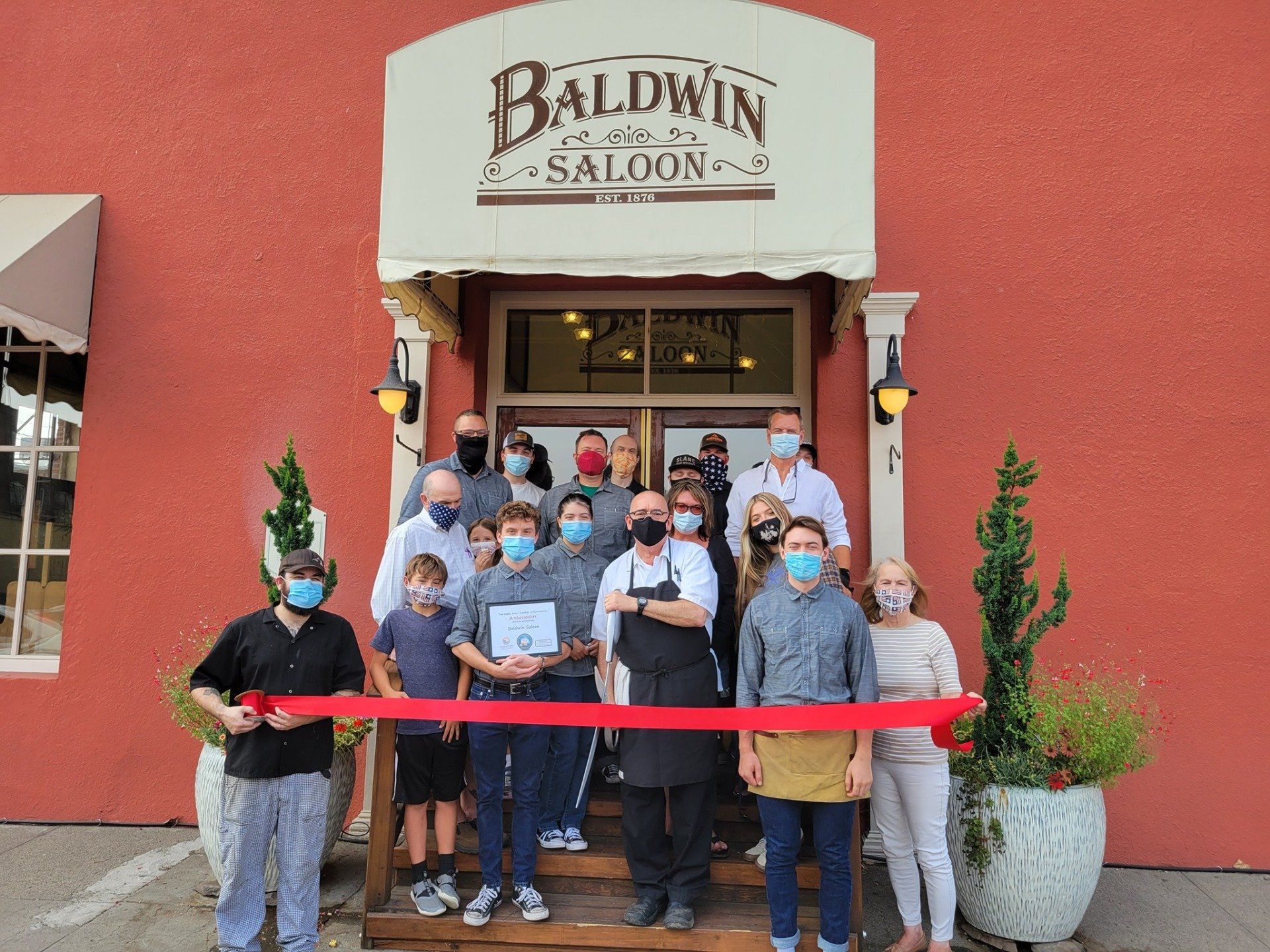 A group of people wearing masks are standing in front of a baldwin saloon.