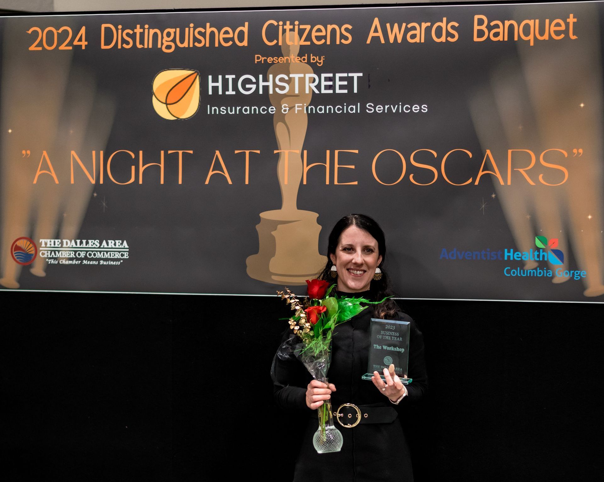 A woman is holding an award in front of a sign that says 2024 distinguished citizens awards banquet