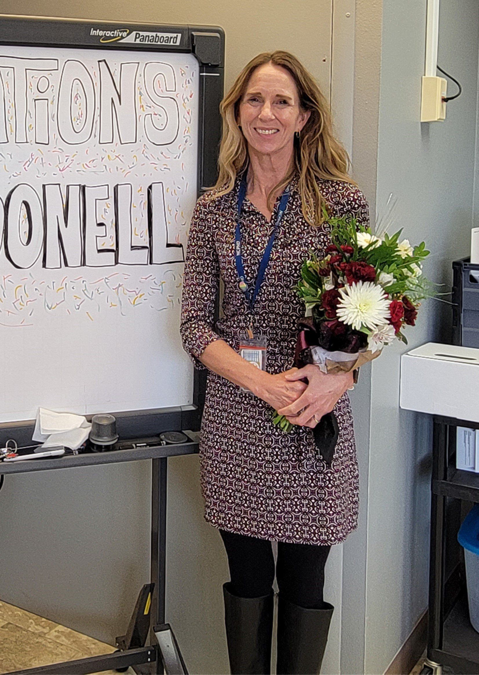 A woman in a dress is holding a bouquet of flowers in front of a white board.