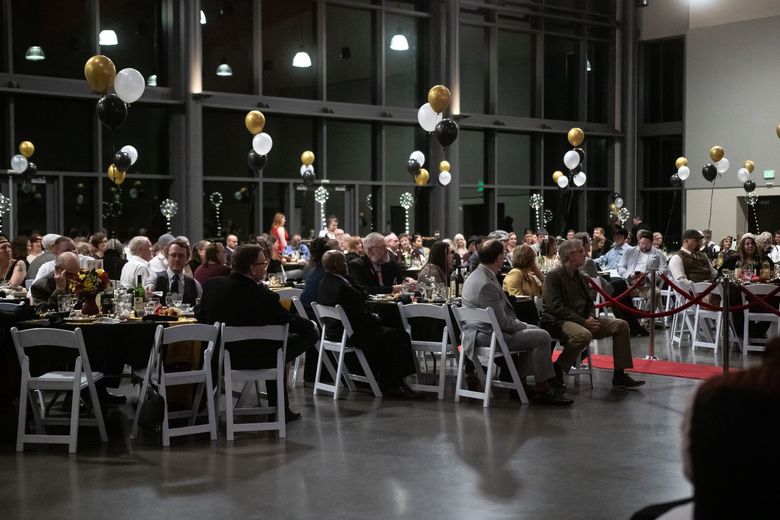 A large group of people are sitting at tables in a large room with balloons hanging from the ceiling.