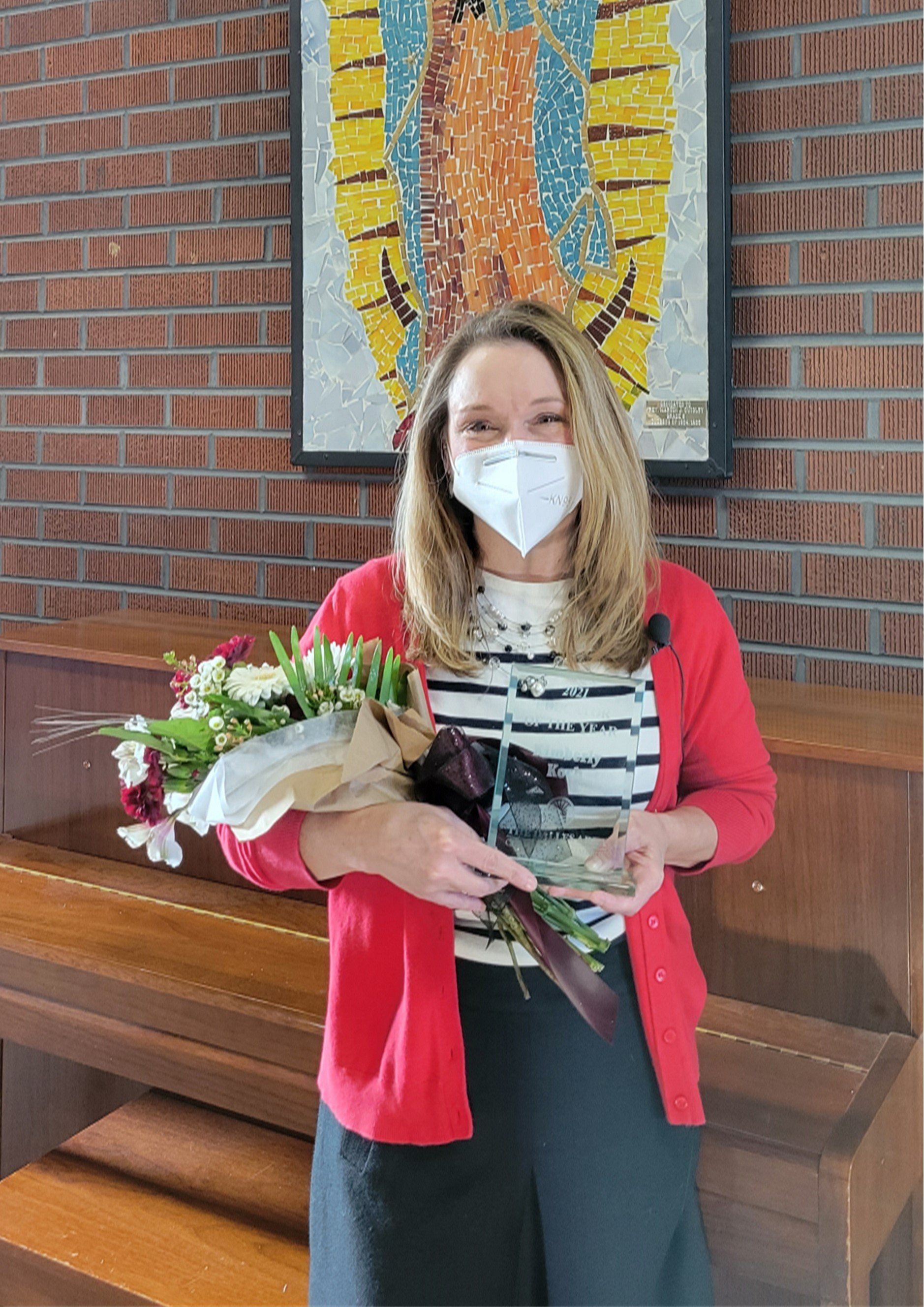 A woman wearing a mask is holding a bouquet of flowers and a trophy.
