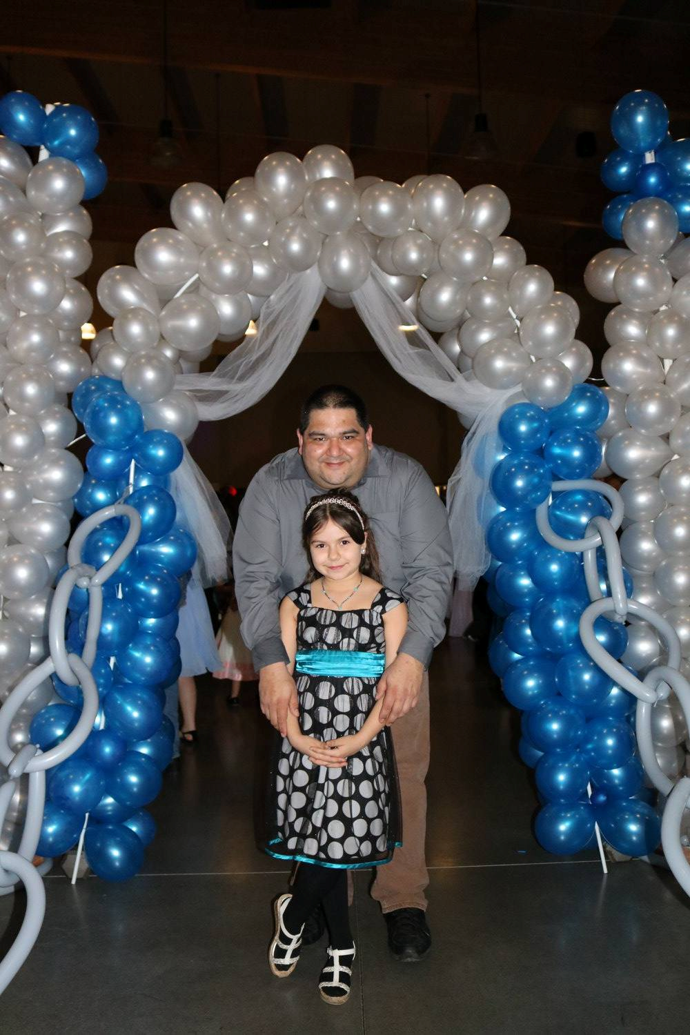 A man and a little girl are standing in front of a balloon arch.