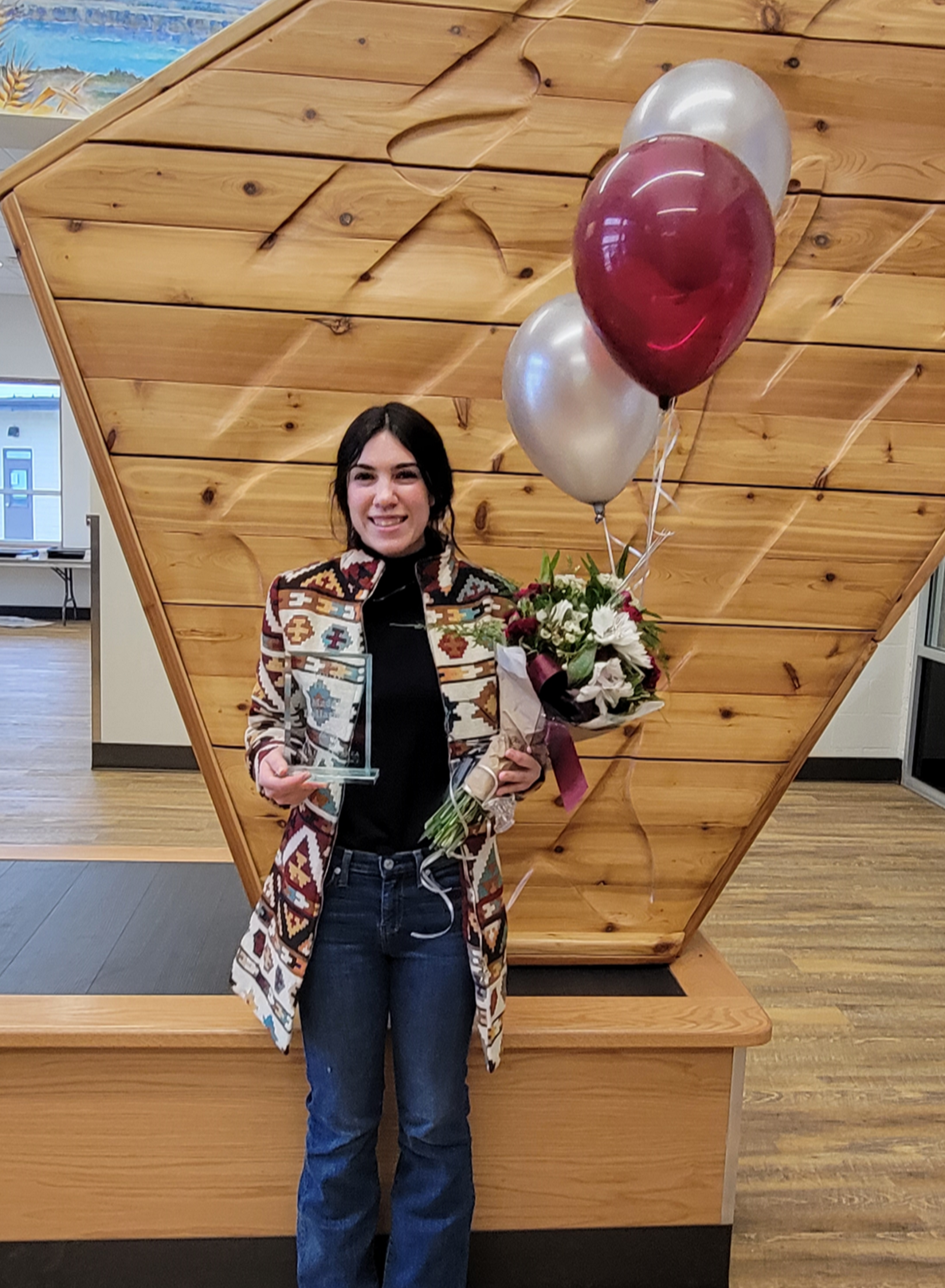 A woman is holding a bouquet of flowers and balloons while standing in front of a wooden wall.