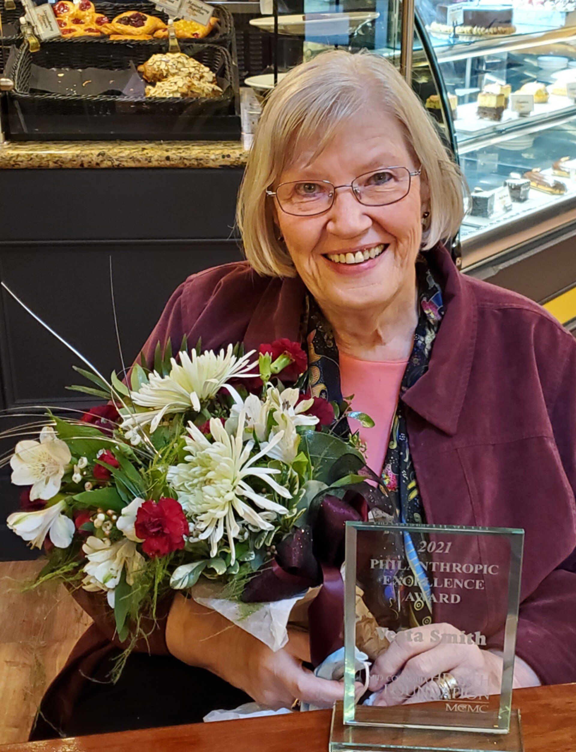 A woman is holding a bouquet of flowers and a trophy.