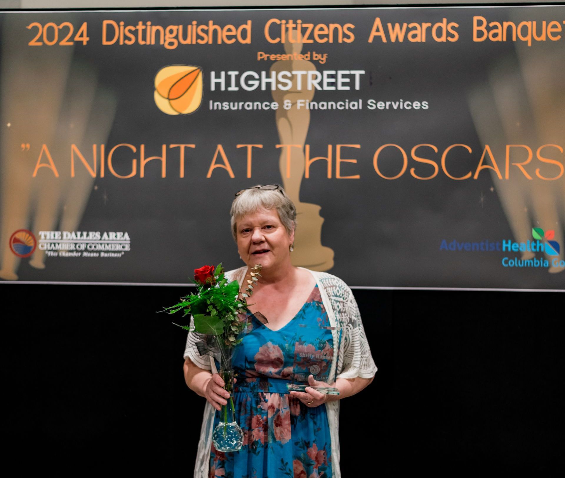 A woman stands in front of a sign that says 2024 distinguished citizens awards banquet