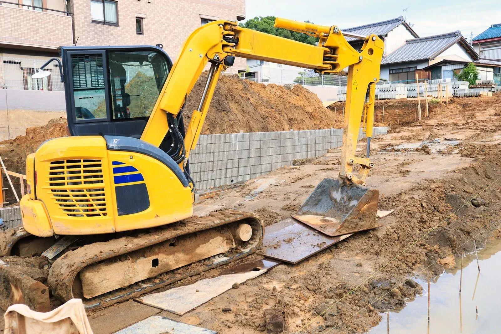 Yellow excavator working at a muddy construction site beside new homes