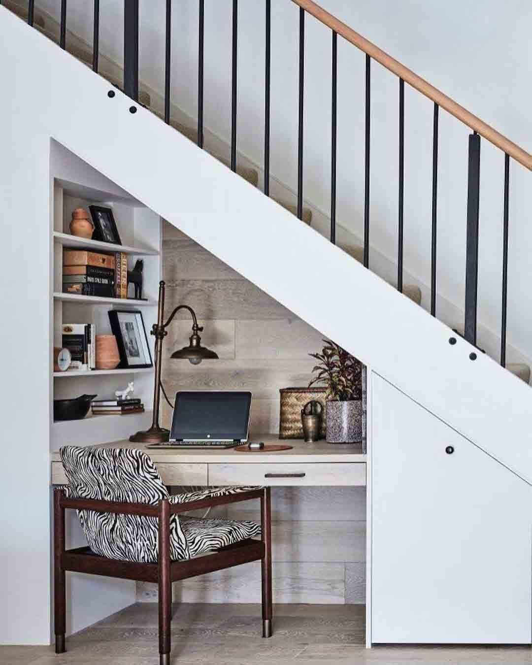 There is a desk under the stairs with a laptop on it.