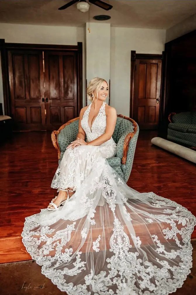 Bride in white lace wedding dress with train, sitting in an ornate chair.
