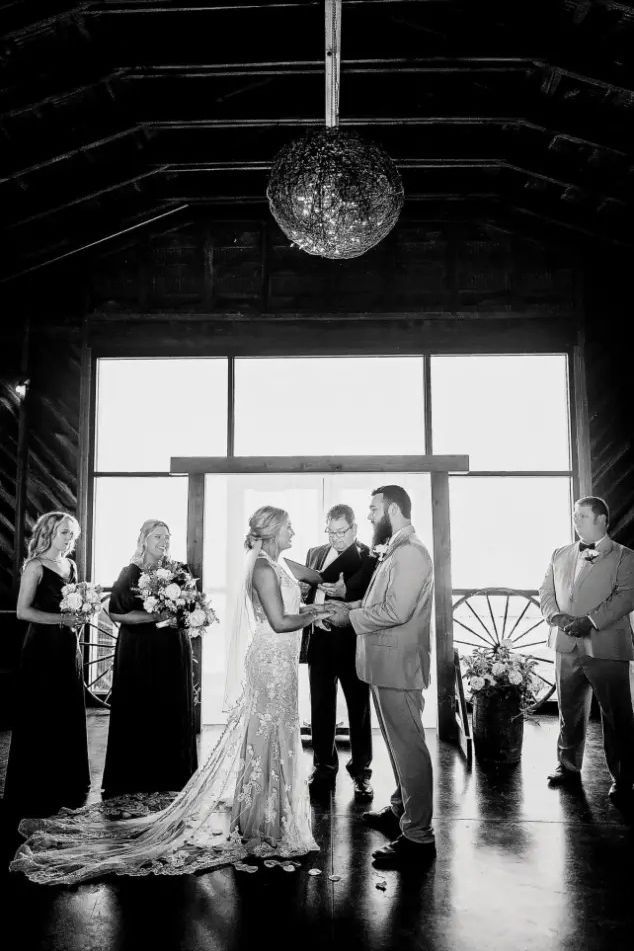 Bride and groom exchanging vows at a wedding ceremony indoors. Guests stand on either side.