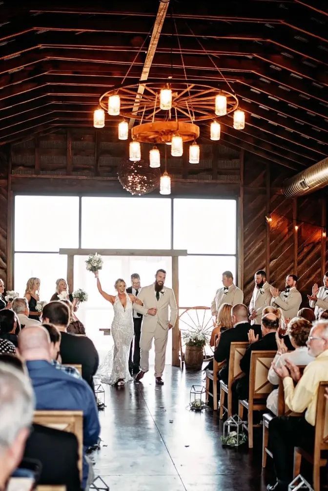 Bride and groom exiting wedding ceremony in a rustic barn, with guests seated on both sides.