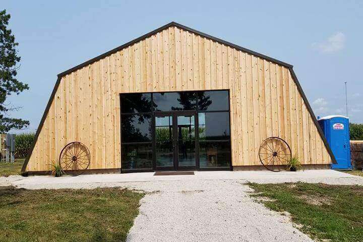 Barn-style wooden building with glass doors, two wagon wheels, and a stone path. Blue sky.
