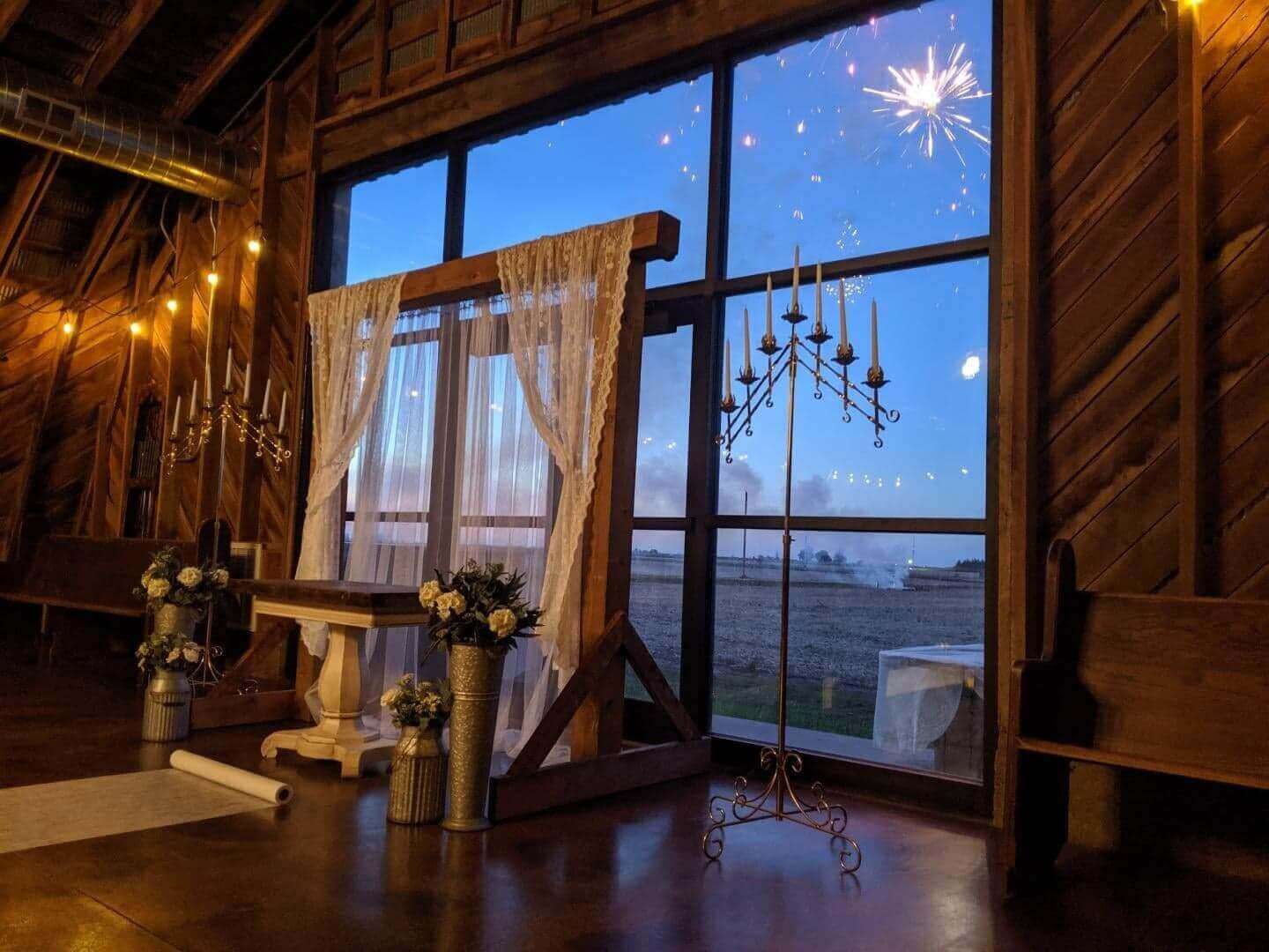 Interior of a rustic venue with a window overlooking a field, altar with curtains, and candlelight.