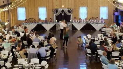Wedding reception: Couple dancing in a large hall with tables and guests. Tables are set, and the bridal party is at a head table.