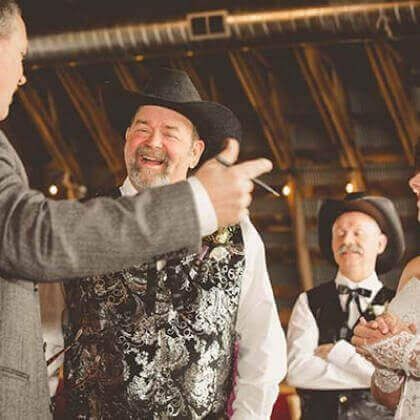 Men in cowboy hats and vests laughing during an outdoor event.