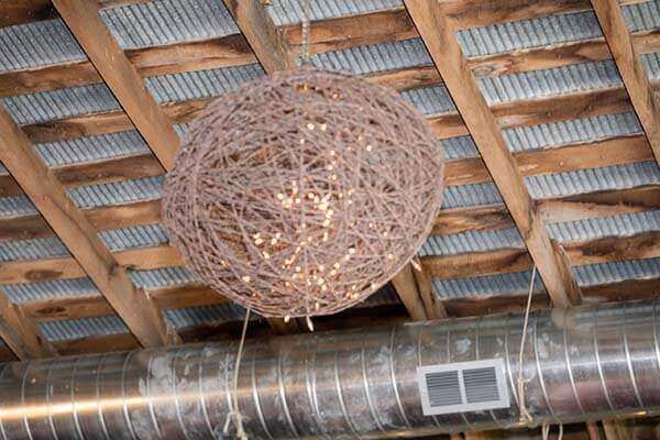 A spherical, vine-covered light fixture hangs from a rustic wooden ceiling, with visible twinkle lights.