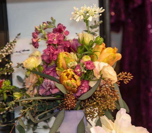 Colorful flower arrangement in a lavender vase, featuring tulips, snapdragons, and other blooms.
