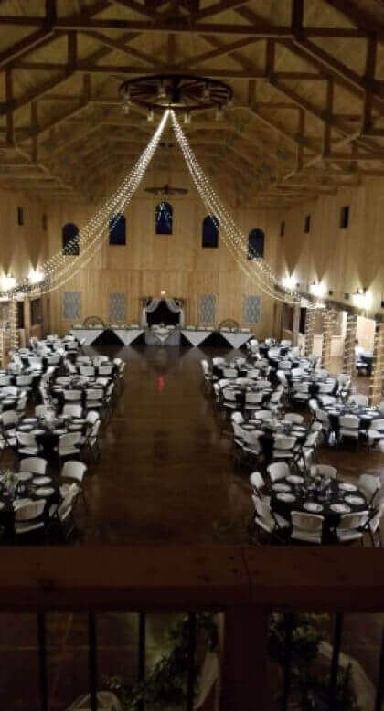 Large event hall with tables set for a gathering, overhead lighting, dark floors, and high ceilings.